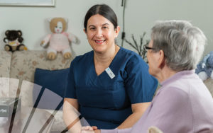 Porträttbild på en undersköterska sittande i soffa bredvid en äldre person med det grafiska elementet solfjädern i hörnet.