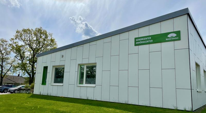 Vitt hus med grön fasadskylt med texten Seniorcenter och Anhörigcenter. Foto.