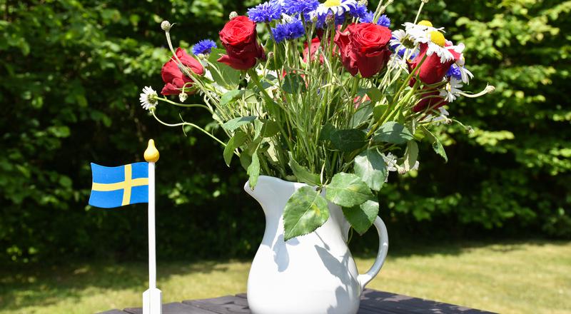 Sommarbukett blommor med svensk flagga på ett bord.